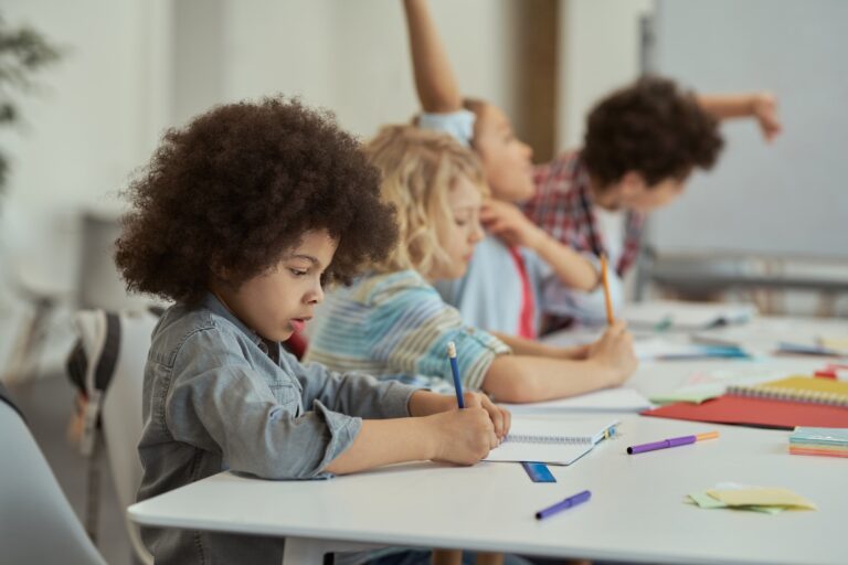 Diligent little schoolboy writing in his notebook while studying, sitting at the table in